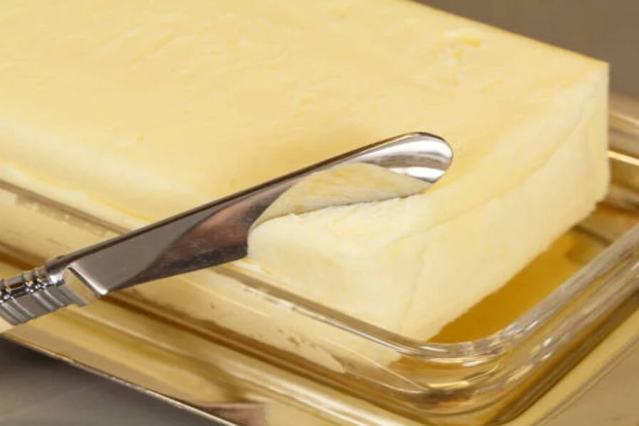 Butter knife cutting through soft butter in glass butter dish
