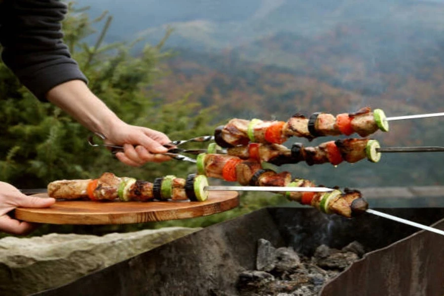 Chef using metal skewers to grill on barbecue outdoors