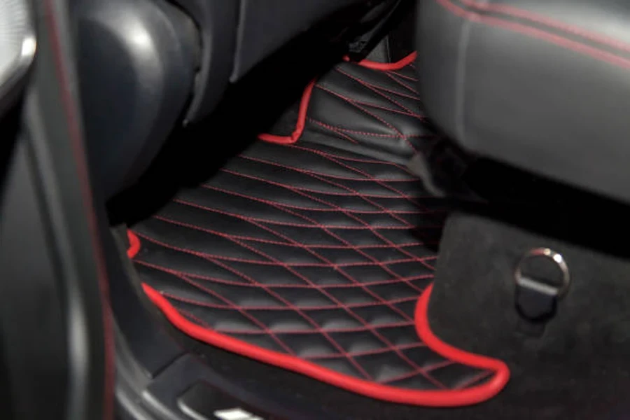 Cleaning black leather car floor mats with diamond red stitching and gas pedal and brake in workshop