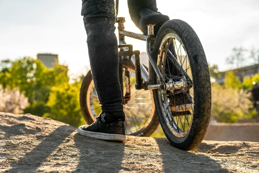 Close-up of a BMX biker standing on dirt in a bright outdoor setting