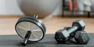 Close-up of ab wheel and dumbbells on a mat in a home gym setting