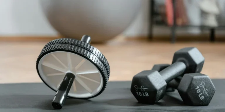Close-up of ab wheel and dumbbells on a mat in a home gym setting