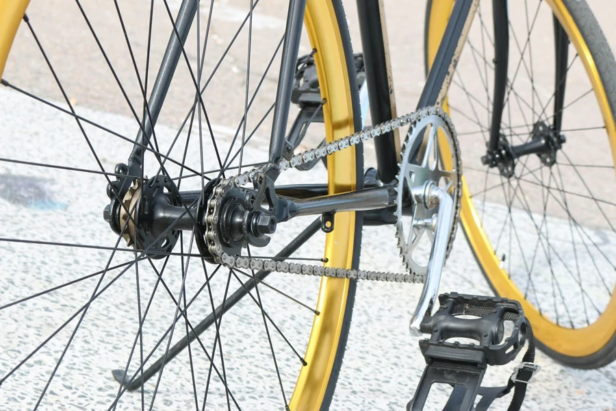 Detailed view of a bicycle chain and gear system with yellow rims in an urban setting