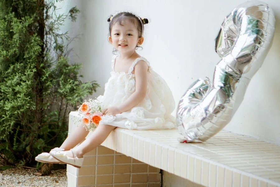 Girl in White Dress Sitting with Birthday Balloon on Bench