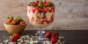 Glasbecher gefüllt mit Erdbeer-Trifle neben einer Schüssel