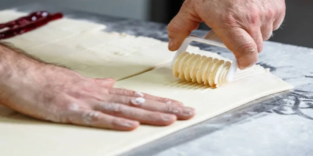 Hand using lattice cutter on pastry dough in kitchen