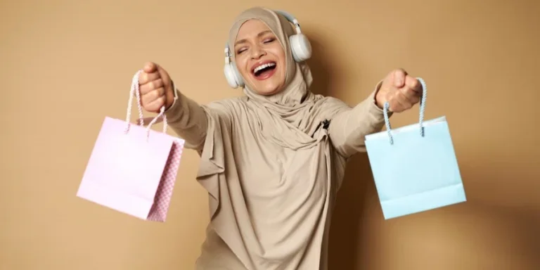 Happy woman in hijab with headphones listening to music and dancing with colored paper bags in her hands enjoying the upcoming religious holidays. Eid Mubarak Said
