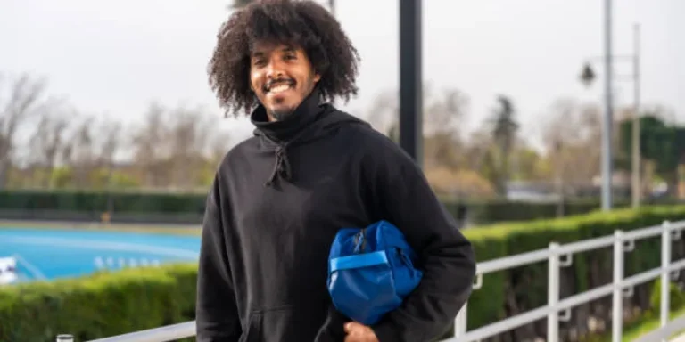 Un homme tenant un sac de pickleball bleu marine sous le bras à l'extérieur des terrains