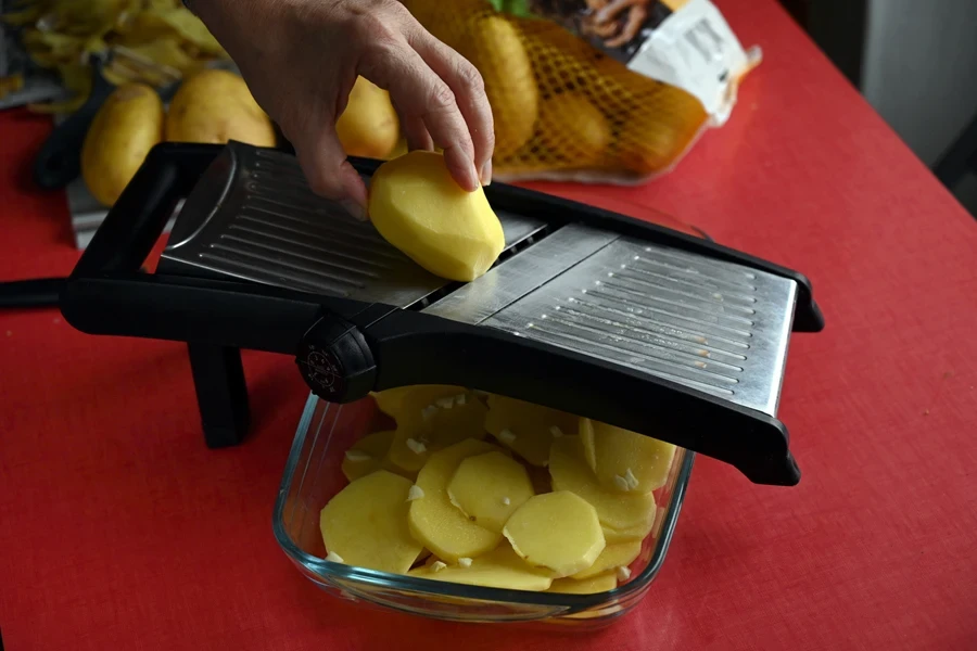 Mandoline cutter slicing potatoes into a transparent container