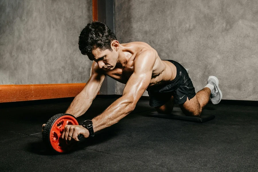 Muscular man exercising with an ab roller for core strength in an indoor gym setting, showcasing athletic fitness