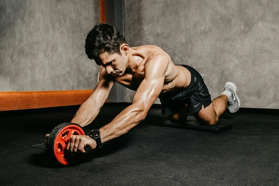Muscular man exercising with an ab roller for core strength in an indoor gym setting, showcasing athletic fitness