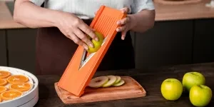 Person slicing apples and oranges using a mandoline slicer