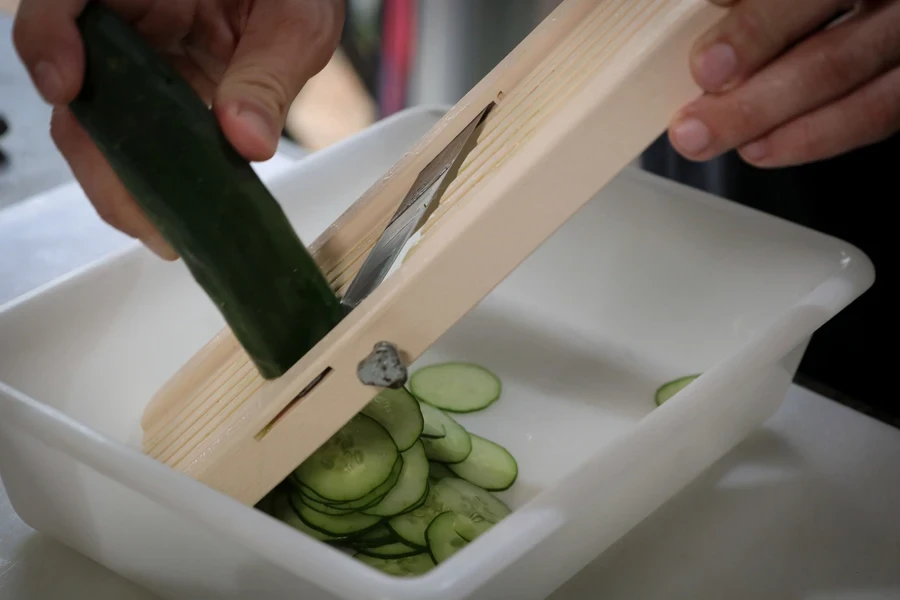 Person using a handheld wooden mandoline slicer to cut cucumbers