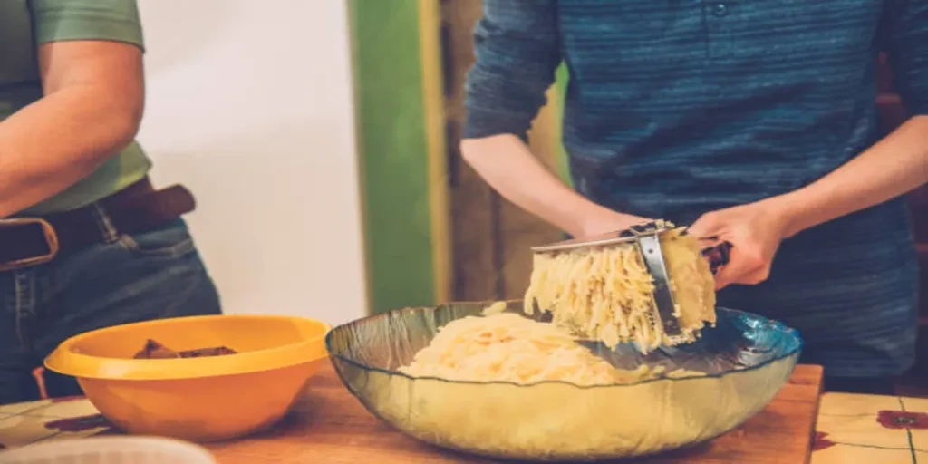 Person using potato ricer to mash potatoes in glass bowl
