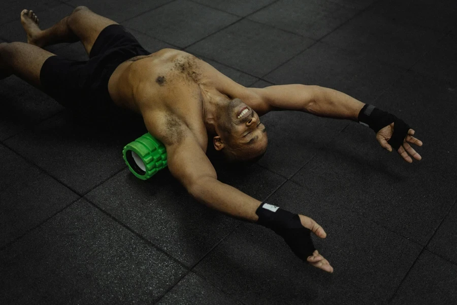 Shirtless man exercising with a foam roller in a fitness center