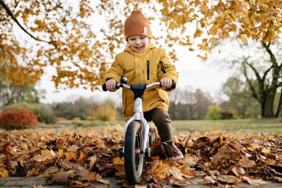 Smiling child in yellow jacket rides a bike through fallen autumn leaves in a park