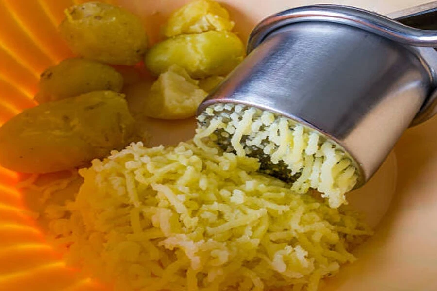 Stainless steel potato ricer sitting in plastic bowl