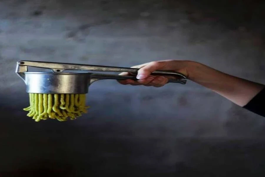 Stainless steel potato ricer with strings of potato coming out