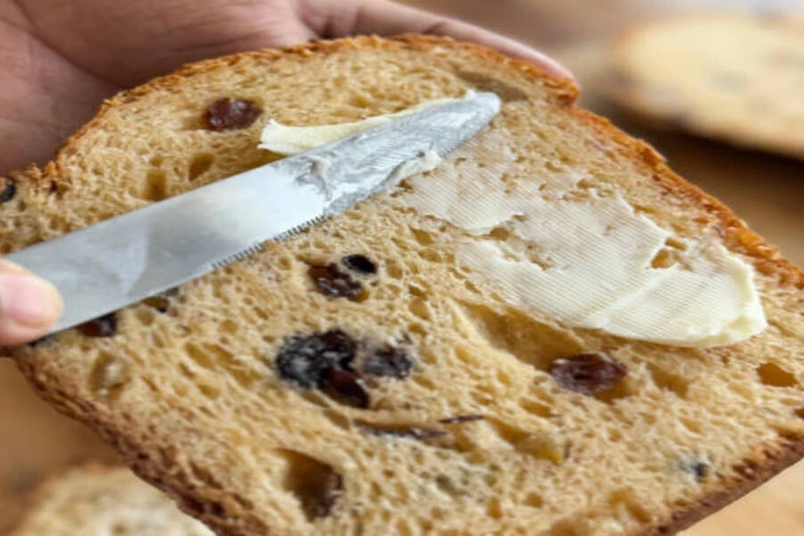 Stainless steel serrated butter knife spreading butter on raisin bread