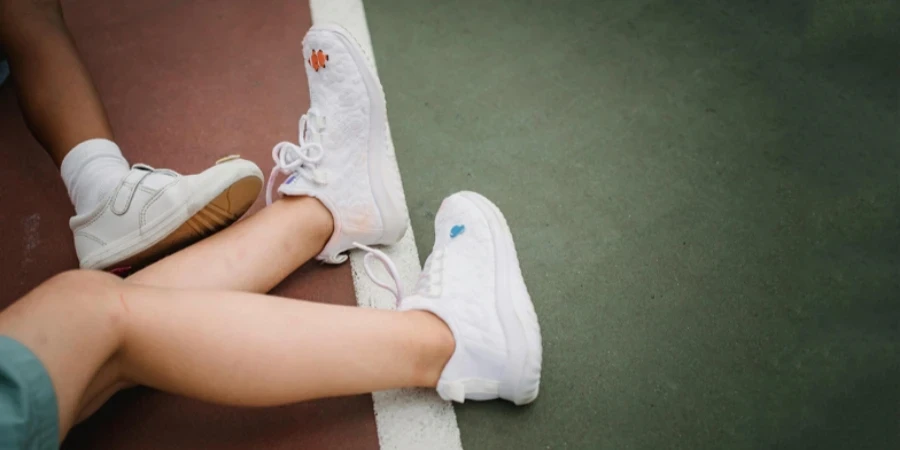 Two children’s legs wearing white sneakers lying on an outdoor sports court