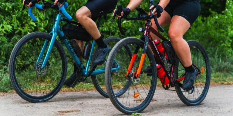 Two cyclists riding gravel bikes on a dirt path surrounded by greenery