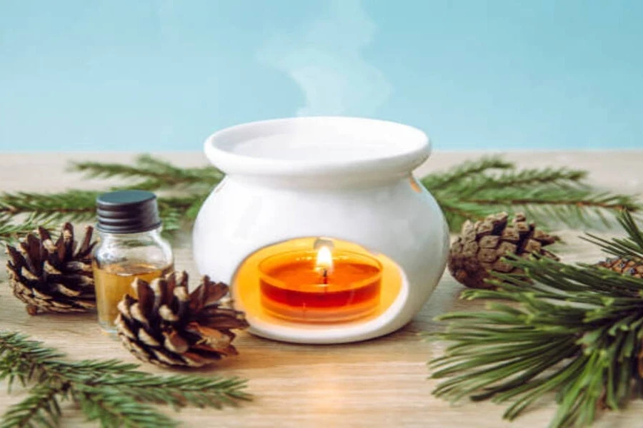 White ceramic wax melter surrounded by pine branches and cones