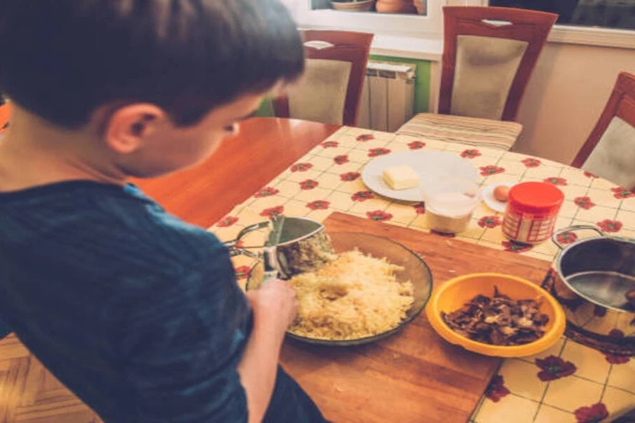 Young boy using press-style potato ricer at dining table