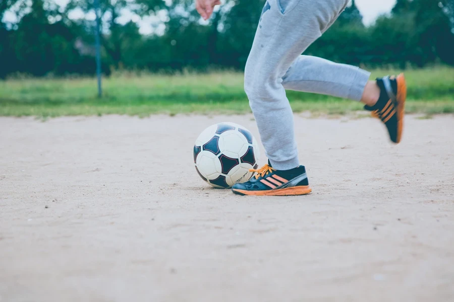 Young player practicing soccer on a sandy outdoor field, capturing motion and fun