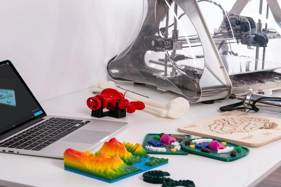 A computer beside a 3D printer with printed models on the table