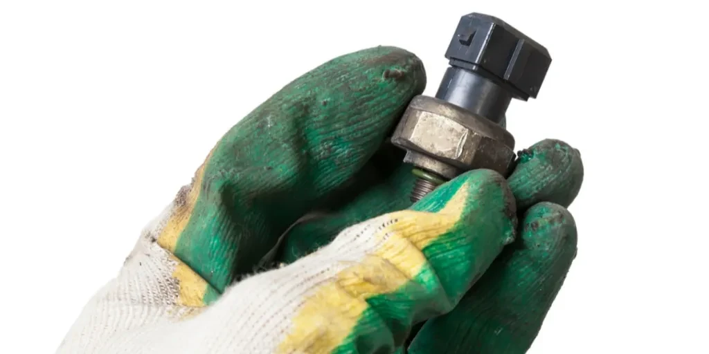 A gloved hand holding an oil pressure sensor