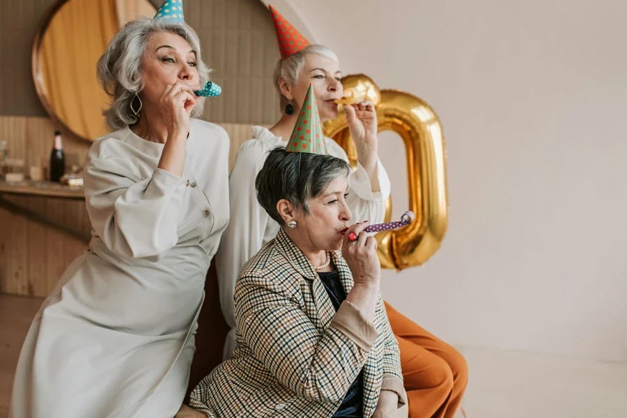 A joyful celebration with senior women in party hats blowing party blowers indoors