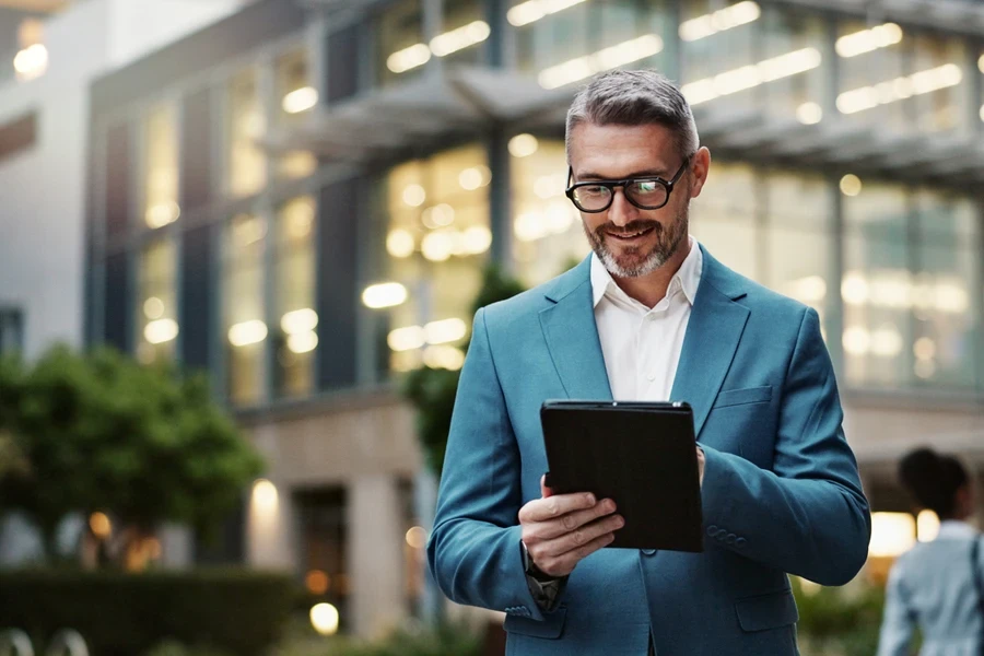 A smiling businessman using a tablet outdoors