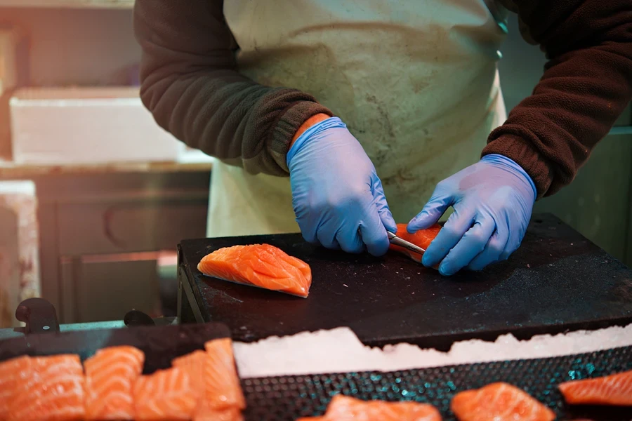 Chef in kitchen using fish knife to debone salmon pieces