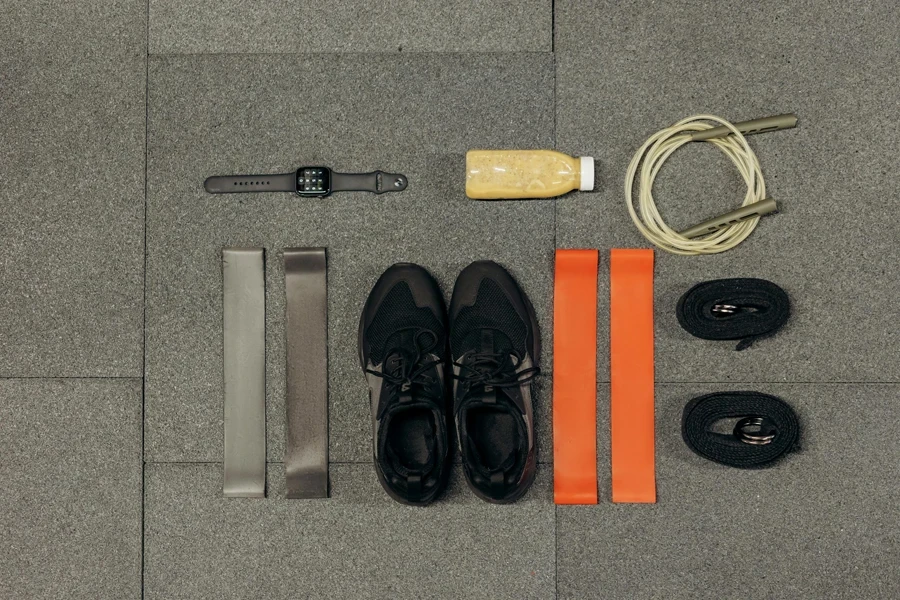 Flat lay of workout essentials including sneakers, bands, watch, rope, and healthy drink