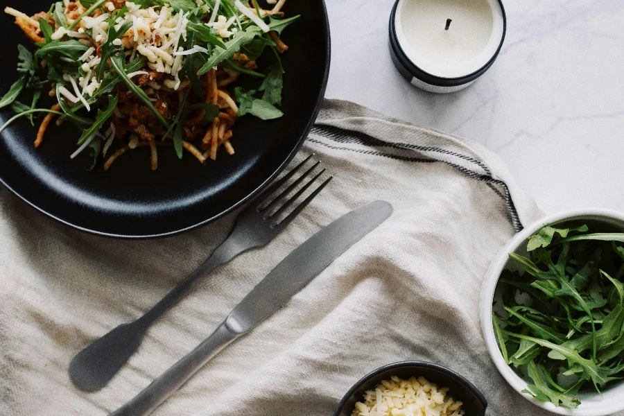 Fresh salad served on black plate with fork and knife on white napkin