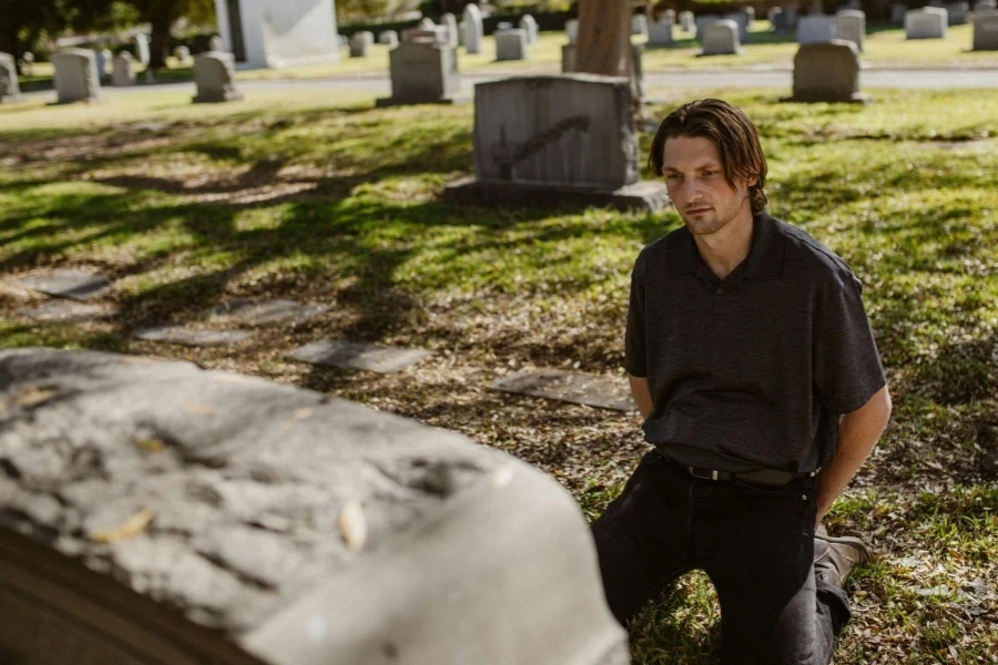 Man in Black Polo Shirt Kneeling In Front of the Tombstone