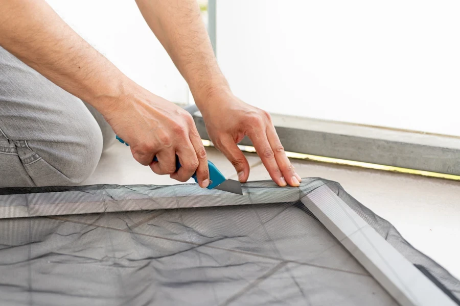 Man using utility knife to cut netting on window frame