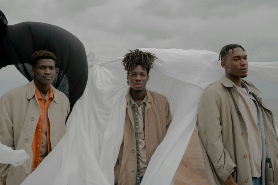 Men in Coats Standing on Beach With White and Black Cloth in Wind