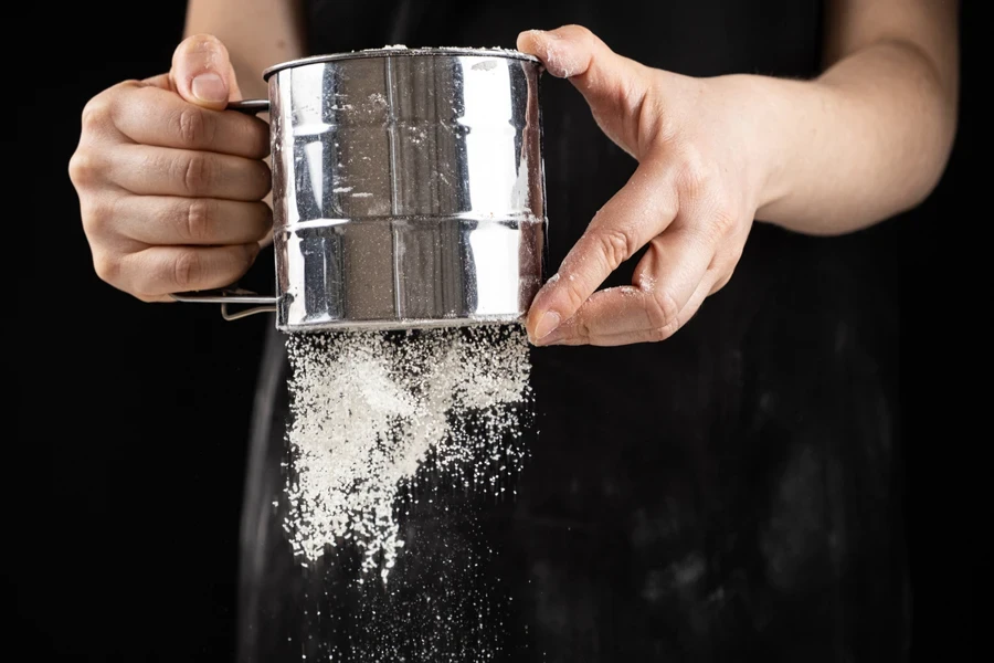 Metal hand-crank sifter with flour flowing from the bottom