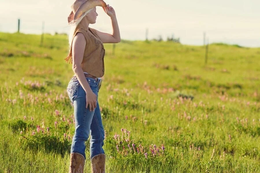 Woman wearing brown cowboy boots, vest, and hat