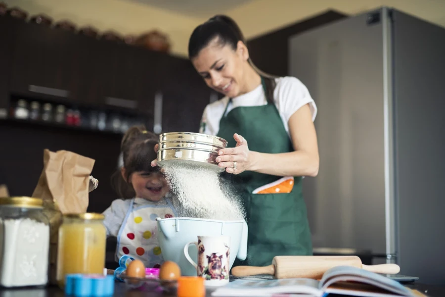 Woman with daughter using bowl sifter in kitchen