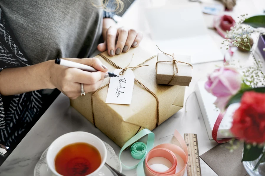 Woman writing a thank you note with a gift on the package
