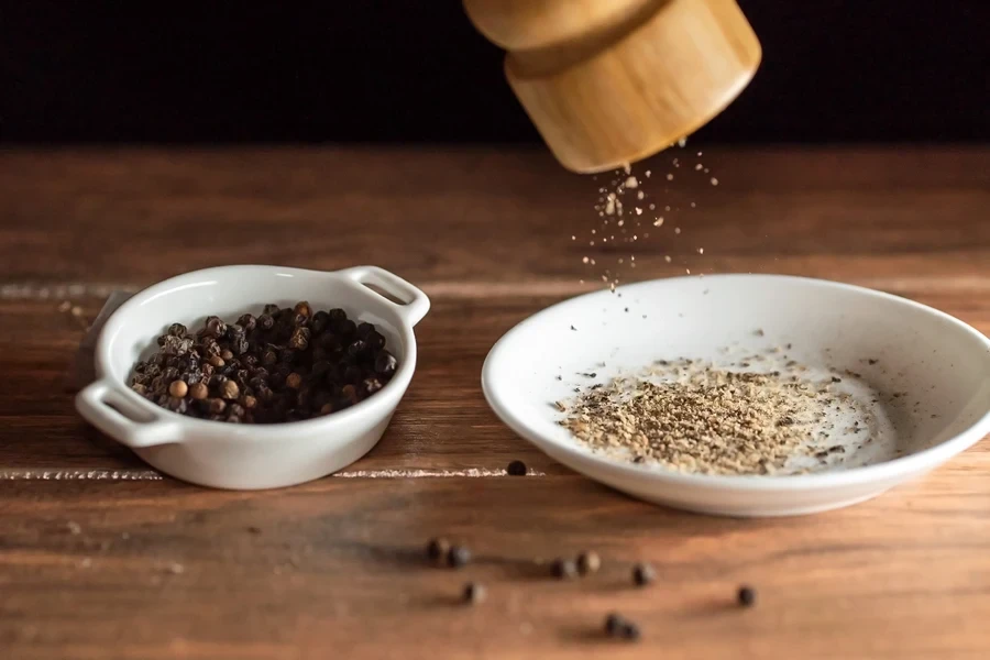 Wooden pepper grinder with ground pepper falling on dish