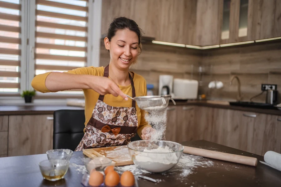Young woman using stainless steel sifter over glass bowl