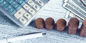A calculator, pen, and money on a table.