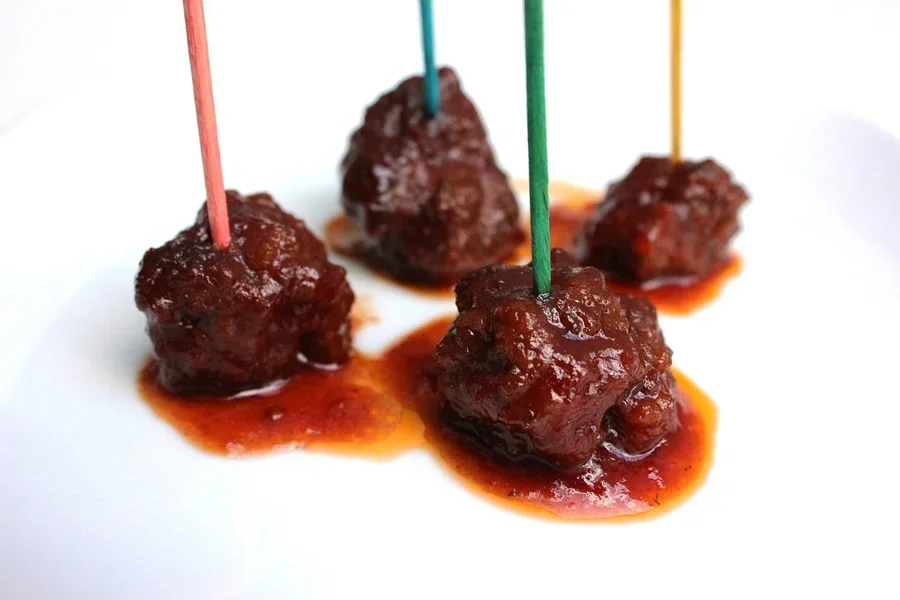 A group of meatballs with sauce on sticks