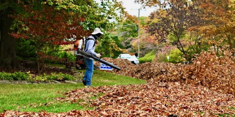 A landscaper wearing a backpack leaf blower blows off leaves