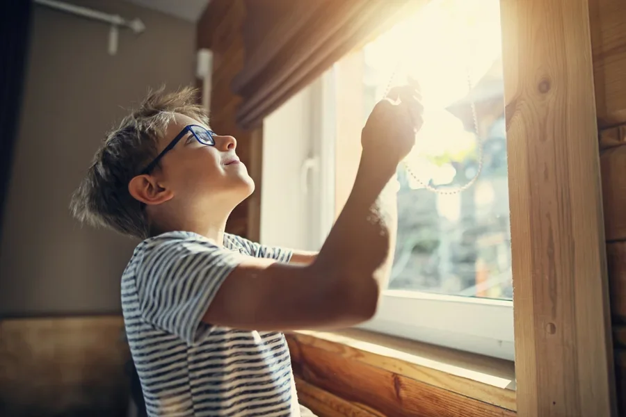 Boy opening window blinds on a sunny day