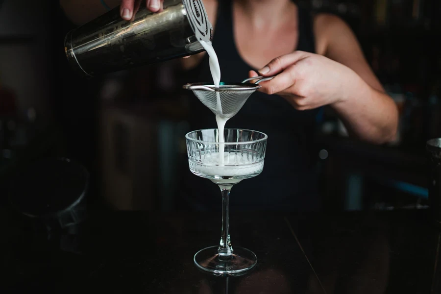 Female bartender using fine-mesh strainer with cocktail in bar