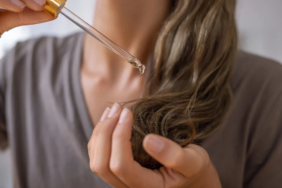 Girl applying dose of hair serum during the day